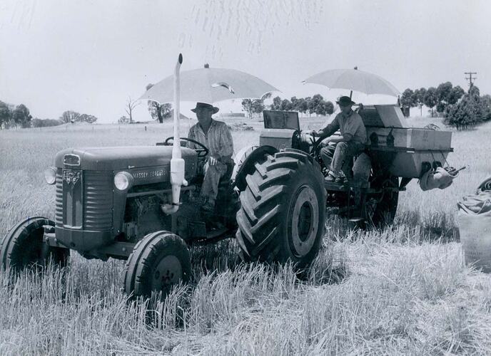 2 men driving a tractor and harvester in field.