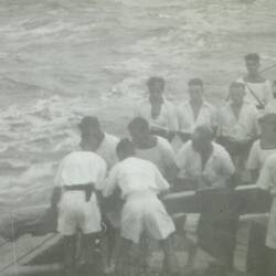 Uniformed sailors on the deck of a ship placing a wrapped body into the ocean.