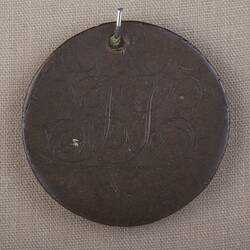 Round copper disc with words inscribed and hole punched at top.