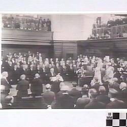 Crowds in a parliamentary chamber, facing a royal representative in Speaker's chair.