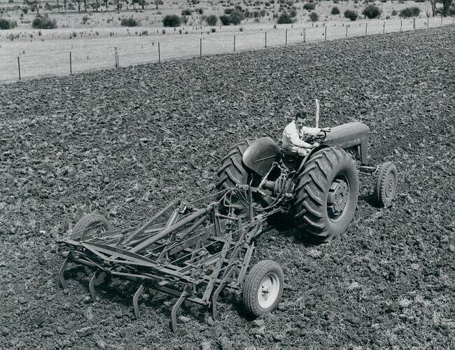 Rear view of a man driving a tractor coupled to a scarifier, in wide open field.