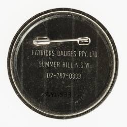 Back of round button badge with a safety pin. Stamped text.