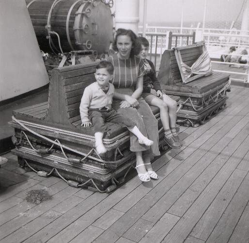 Woman and two children seated on ship deck.