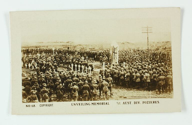 Crowd of servicemen standing in graveyard, flag in centre.