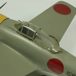 Green grey plane model with red spot on each wing and fusleage. Yellow nose, black propeller. Cockpit detail.