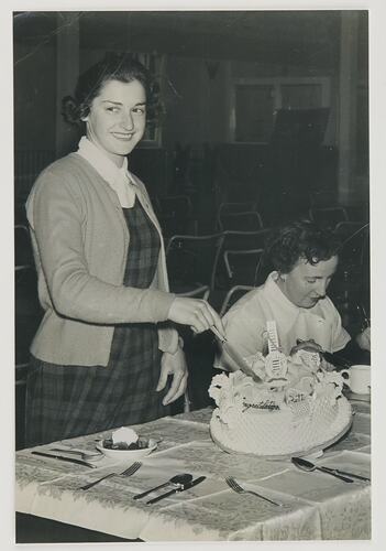 Woman wearing a tartan dress and cardigan cutting a 21st birthday cake.