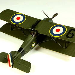 Dark green model airplane. Circle pattern on top on each wing. Rear right view.