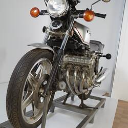 Silver motor cycle. Single headlight, round silver side mirrors and orange indicators.