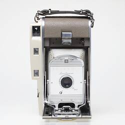 Off-white fold out camera, taupe cover, metal trim. Has bellows, leather strap.