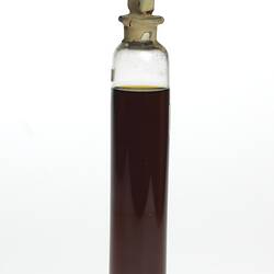 Cylindrical glass jar with dark brown liquid. One label affixed, sealed at top.