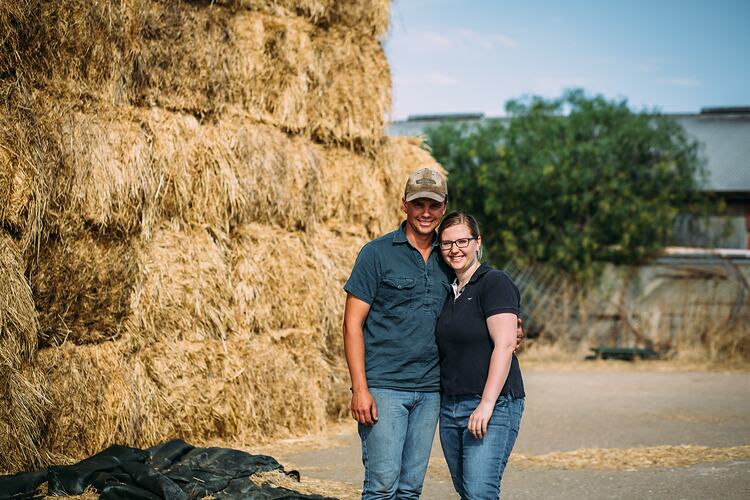 Woman and man in front of a large hay stack.