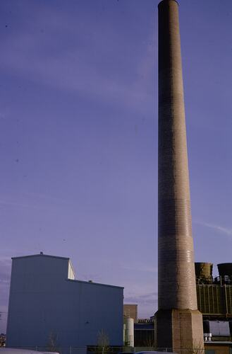 Tall, brick chimney stack beside factory building.