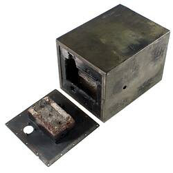 Black metal box (burnt) with flat metal end section (with a hole) beside it.