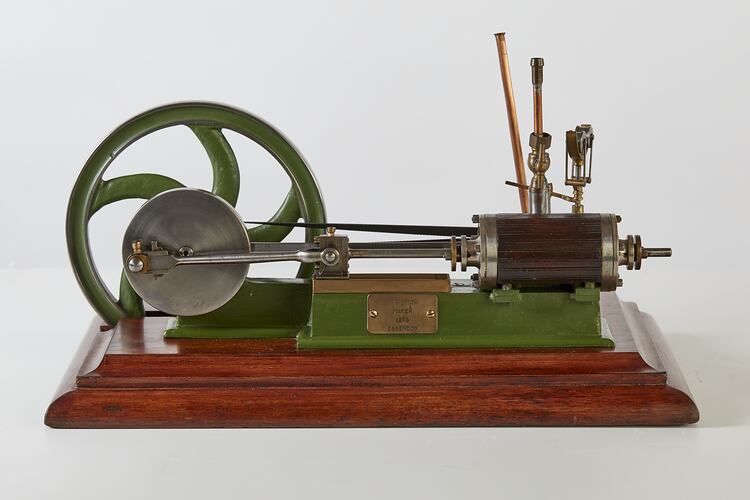 Metal model with large wheel and piston. Green painted frame, wooden base.