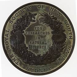 Medal with text framed by wreath. Text around wreath.