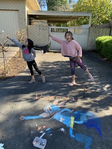 Two girls posing in driveway with chalk drawing in foreground.