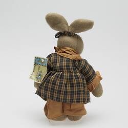 Soft toy rabbit dressed in brown checked dress. Back view has tag.