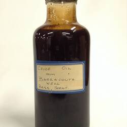 Dark glass jar containing crude oil sample. Off white labelhas handwritten text.