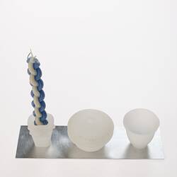 Opaque glass set on metal tray. Candle holder with woven blue white candle, lidded spice container and cup.