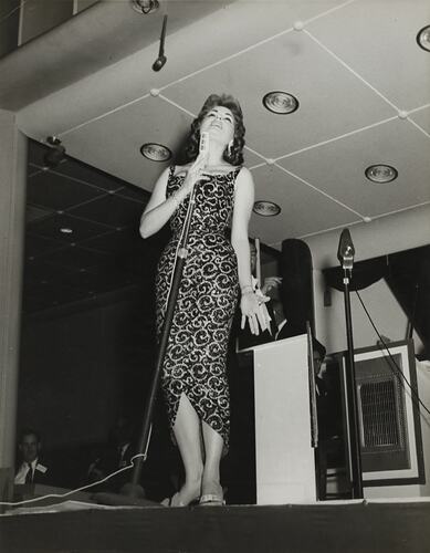 Female performer standing on stage with a microphone.