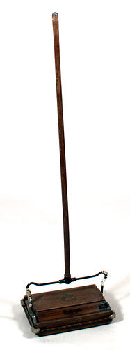 Carpet sweeper, wooden handle and sweeper pan, shown upright. Base has colour logo and text.