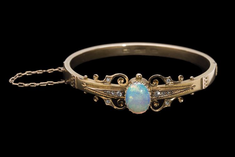 Gold bracelet with central oval white opal, supported by rose cut diamonds and delicate gold filigree-style detail.