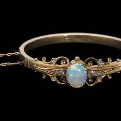 Gold bracelet with central oval white opal, supported by rose cut diamonds and delicate gold filigree-style detail.