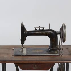Detail of sewing machine fitted to a metal frame with a wooden bench.