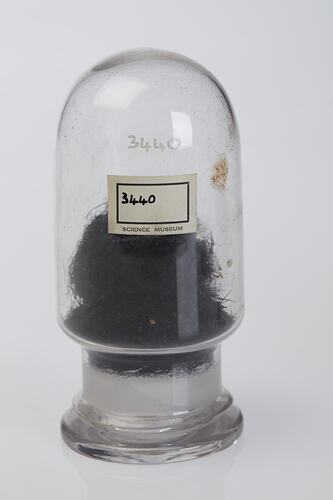 Domed cylindrical jar, labelled, containing black stringy botanical sample.