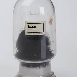Domed cylindrical jar, labelled, containing black stringy botanical sample.