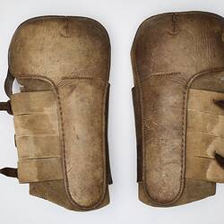 Tan coloured leather shin pads fastened with three dark brown leather straps and buckles.