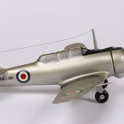 Silver model aeroplane. Red, white, blue roundels on wings and body. Flag on tail. Black propeller and wheels.