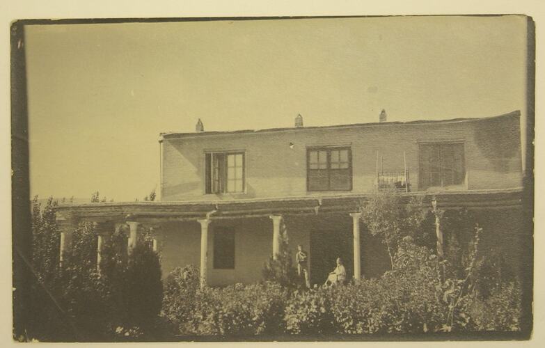 house with two people on porch, one seated, one standing.