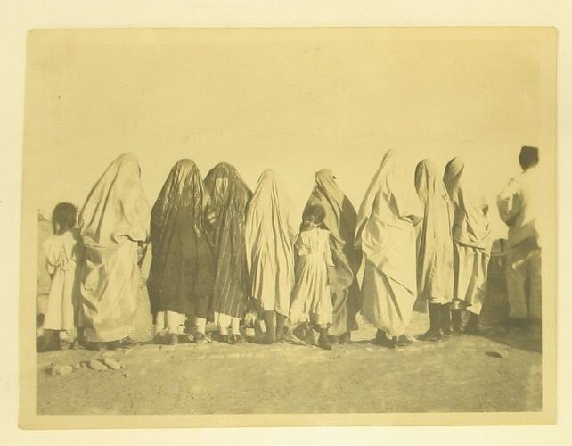 Backs of group of women, all wearing Burkas or Chadors, and children.