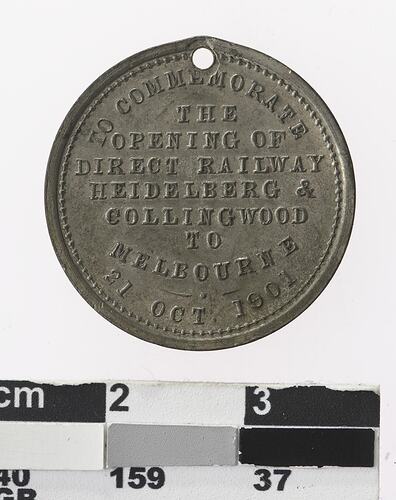 Round silver coloured medal with text.