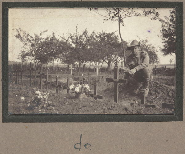 Servicemen in a graveyard kneeling before a grave with trees in the background.