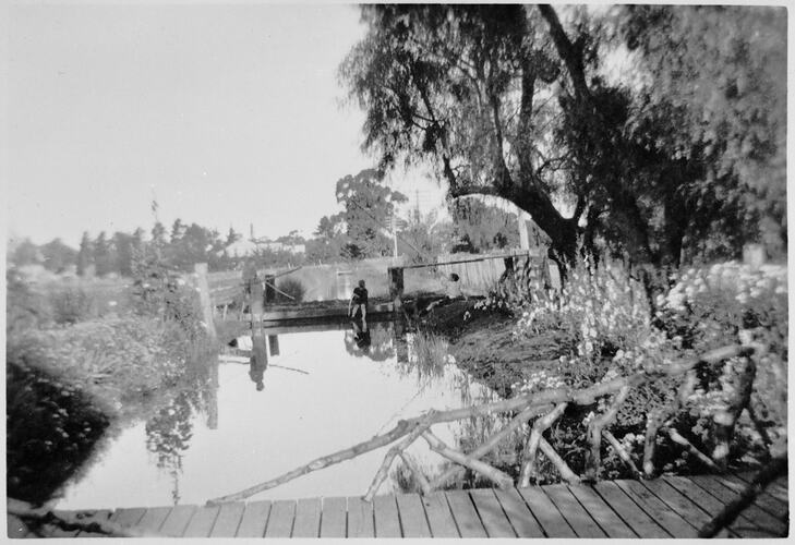 View from bridge over channel towards a set of sluice gates. Someone is standing on the gates.
