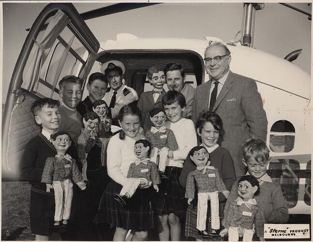 Two adults and a group of children holding ventriloquist dolls.