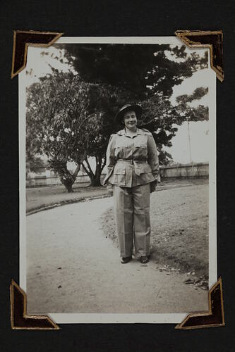Woman in uniform standing on path with trees and picket fence in background.