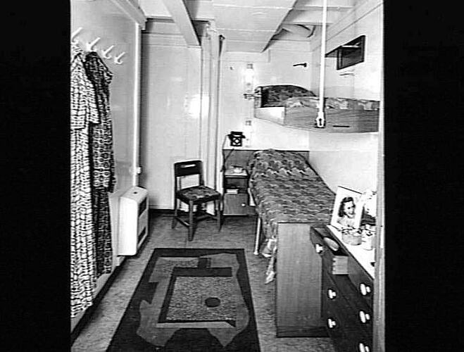 Ship interior. Single bunk beds on right wall. Chest of drawers at right.