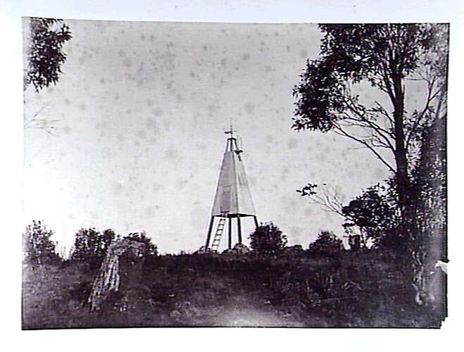 Wooden pyramid structure on hill, with trees.