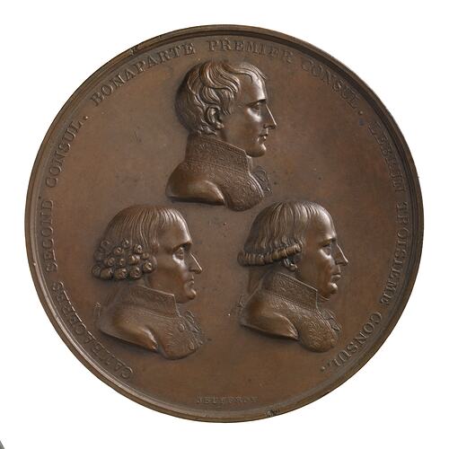 Round medal with three male profiles facing right.