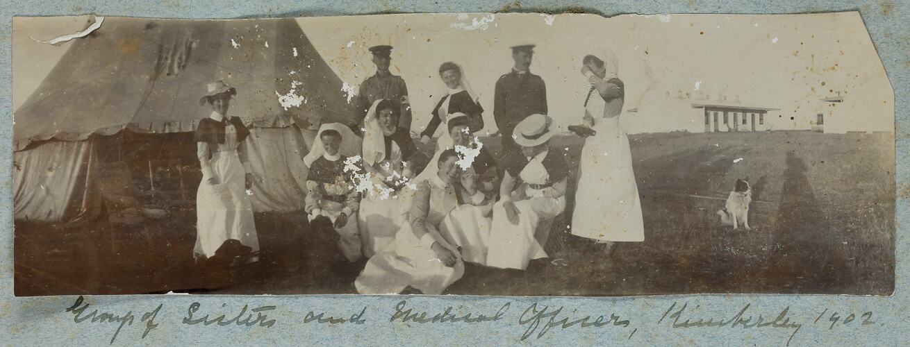 Group of ten people, with woman in nursing uniform and men in military uniform, tent behind.