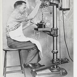 Photograph of man working at drill press.