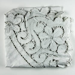 Folded detail of white cutwork embroidery.