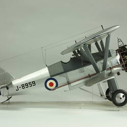 Silver model biplane model with red, white, blue rondels on wings and fuselage. Silver propeller. Profile.