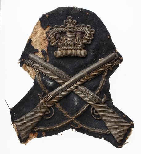 Worn navy blue felt cloth badge with gold embroidered crown above muskets.