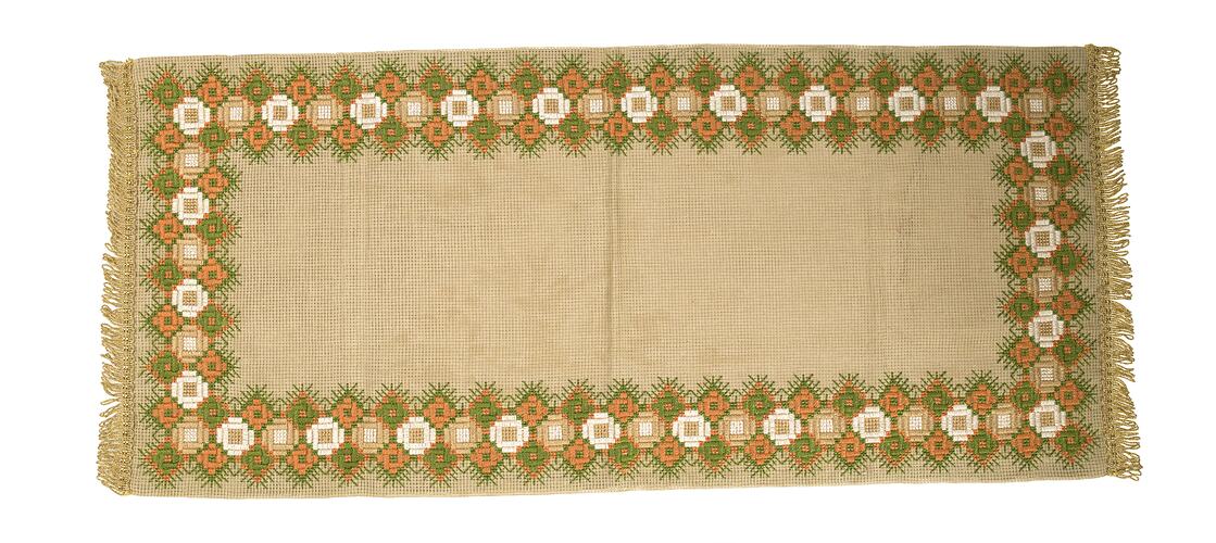 Rectangular cream cloth table runner with orange, green and white floral design. Gold fringing on ends.