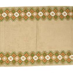 Rectangular cream cloth table runner with orange, green and white floral design. Gold fringing on ends.