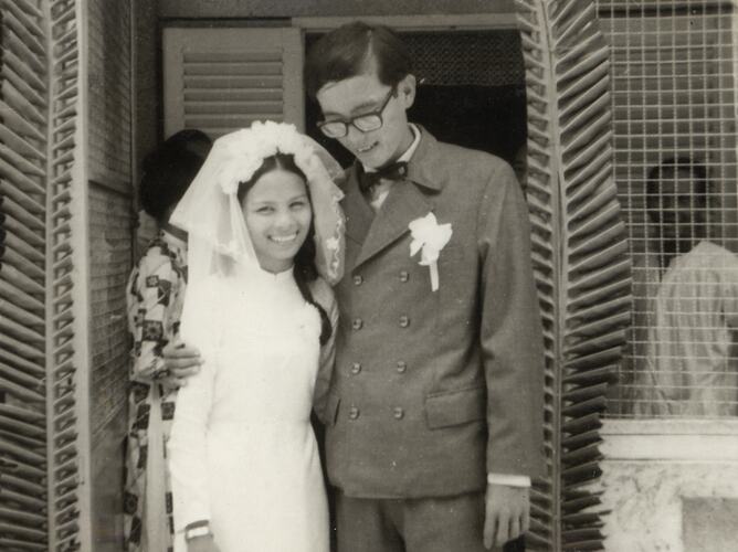Man and woman dressed in wedding attire stand in a doorway.